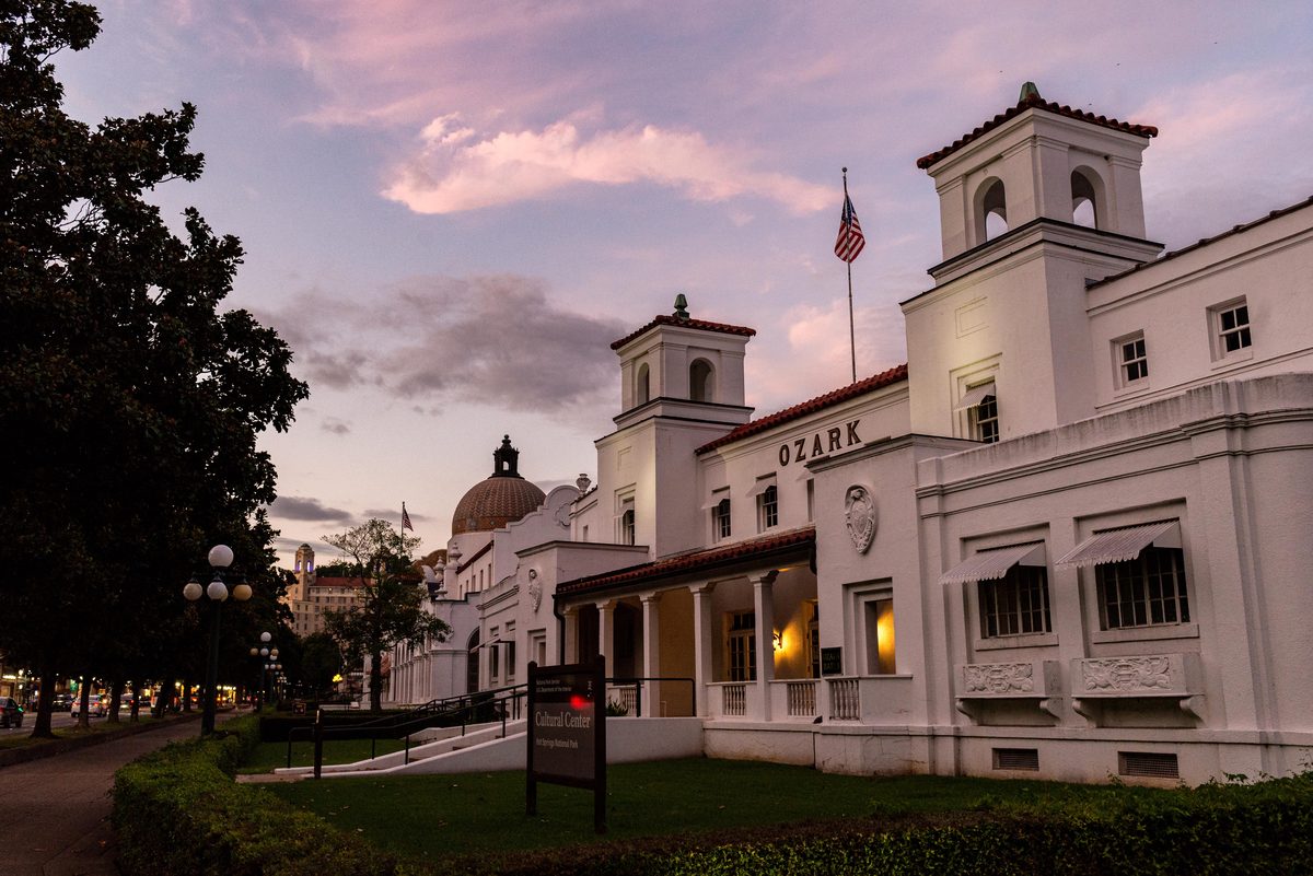 Bathhouse Row at Hot Springs National Park, Arkansas — a line of stately white historic bathhouse buildings beneath a soft pink and lavender sunset sky, the row's columned facades catching the last warm light against the deepening dusk.